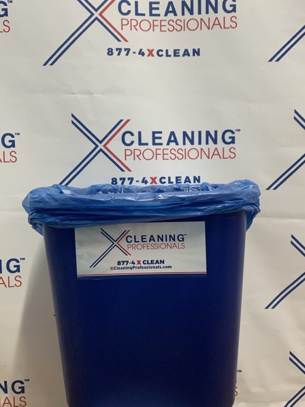 A blue Box of 8 Gallon Trash Liner in front of a sign that says x cleaning professionals.