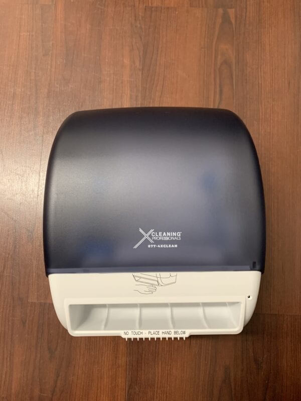 A blue and white X Automatic Towel Dispenser sitting on a wooden floor.